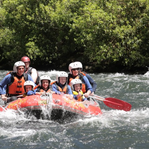 Group rafting on a river, all wearing helmets and life jackets.