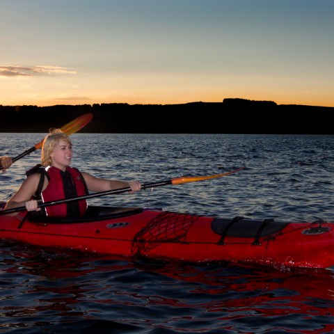 Two people kayaking on a lake at sunset with hills in the background.