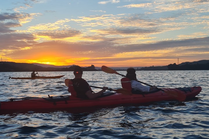 People kayaking on a lake at sunset with a vibrant sky.