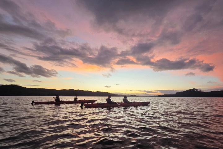 People kayaking on a lake under a colorful sunset.